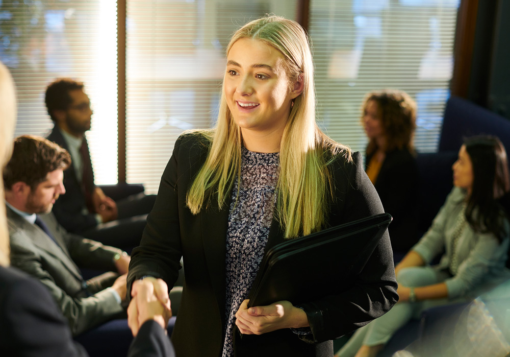 Young woman in a blazer shaking hands in an office.