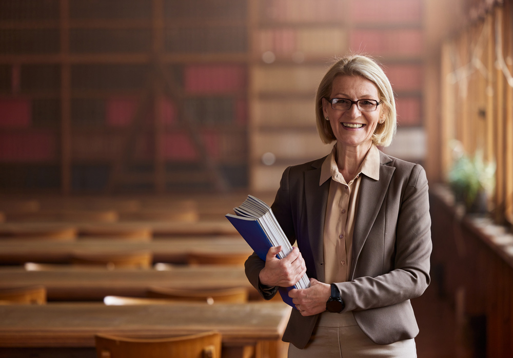 Person holding blue binders, standing in a library with bookshelves and tables.
